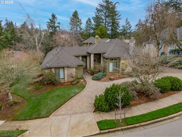 view of front of property with a chimney, brick siding, decorative driveway, and a front yard