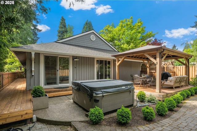 rear view of property featuring a hot tub, a deck, a gazebo, and fence