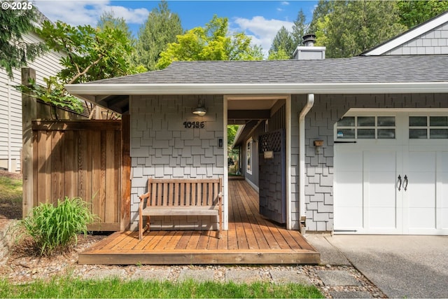 view of exterior entry featuring roof with shingles, an attached garage, and a chimney