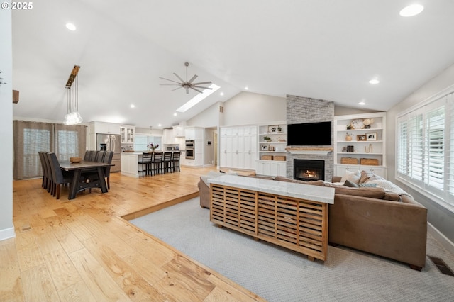 living room with vaulted ceiling, a fireplace, light wood-type flooring, a ceiling fan, and recessed lighting