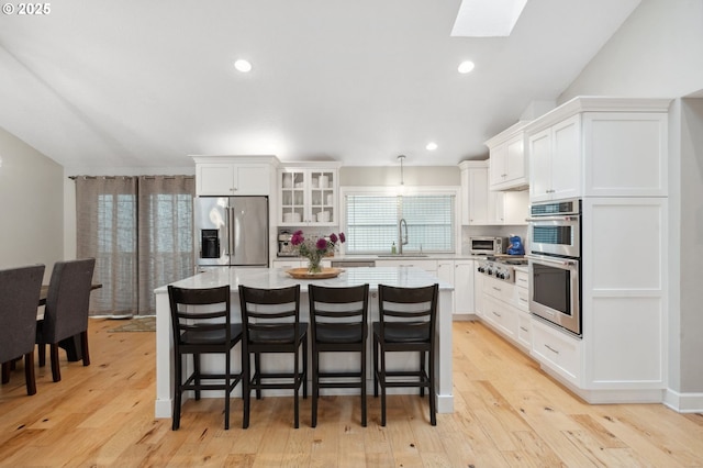 kitchen featuring appliances with stainless steel finishes, a sink, a skylight, a center island, and white cabinetry