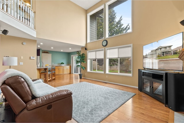 living room with recessed lighting, baseboards, a high ceiling, and wood finished floors