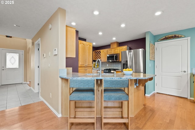 kitchen featuring a peninsula, a sink, light wood-style floors, appliances with stainless steel finishes, and backsplash