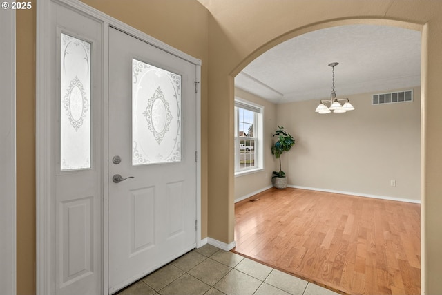 foyer entrance with light tile patterned floors, visible vents, baseboards, arched walkways, and a notable chandelier