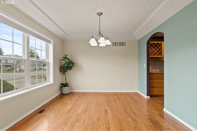 unfurnished room with visible vents, baseboards, light wood-type flooring, and an inviting chandelier