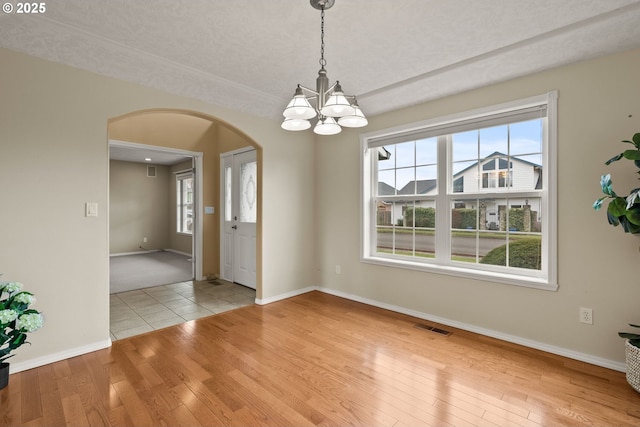 unfurnished dining area featuring hardwood / wood-style floors, plenty of natural light, arched walkways, and visible vents