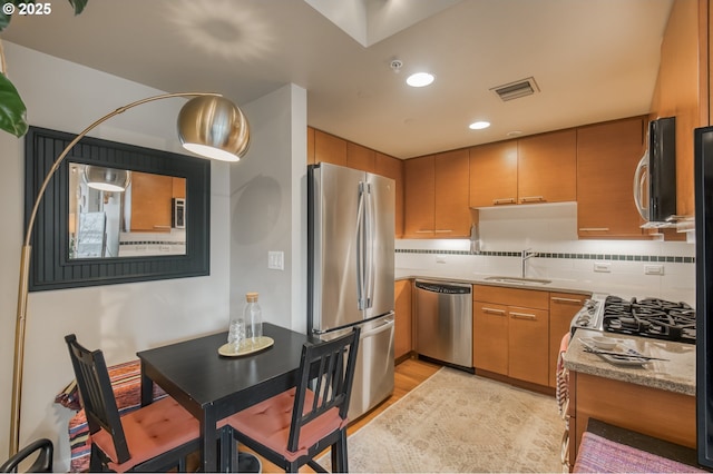 kitchen with visible vents, light wood-style flooring, a sink, stainless steel appliances, and backsplash