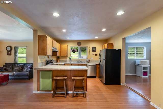 kitchen with appliances with stainless steel finishes, a peninsula, a sink, tile counters, and light wood-style floors