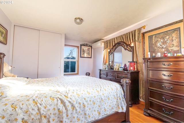 bedroom with a wall mounted air conditioner, light hardwood / wood-style floors, and a closet