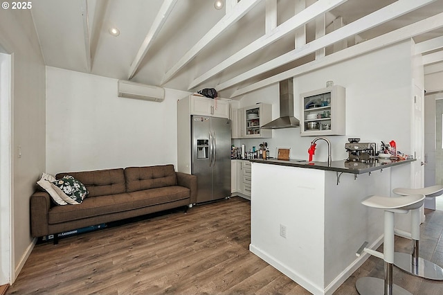 kitchen featuring a breakfast bar, dark countertops, stainless steel fridge, a peninsula, and wall chimney exhaust hood