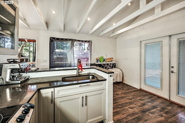 kitchen featuring dark countertops, vaulted ceiling with beams, stovetop, dark wood-style floors, and a sink