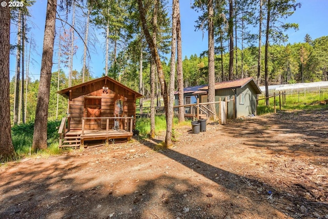 back of house with an outdoor structure, fence, and a forest view