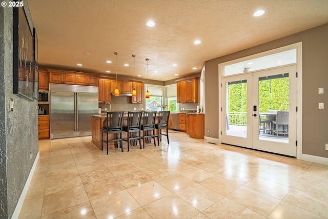 kitchen with stainless steel appliances, baseboards, brown cabinetry, recessed lighting, and an island with sink