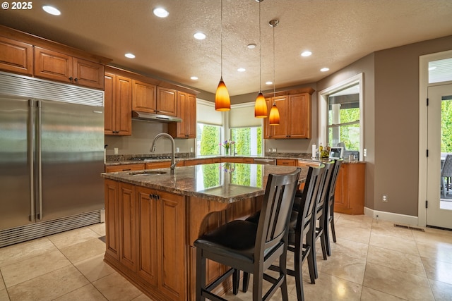 kitchen with appliances with stainless steel finishes, brown cabinets, recessed lighting, a textured ceiling, and under cabinet range hood