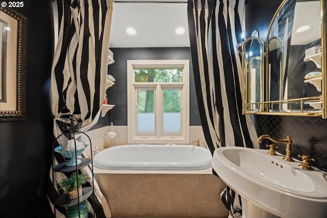 bathroom with a relaxing tiled tub, sink, and decorative backsplash