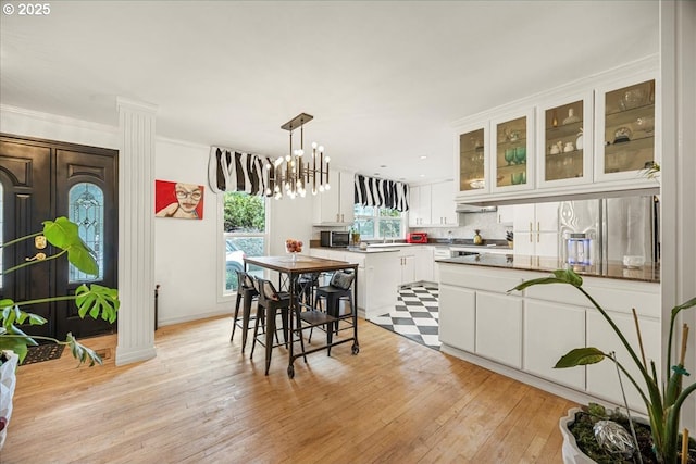 kitchen featuring white cabinetry, hanging light fixtures, light wood-type flooring, appliances with stainless steel finishes, and backsplash