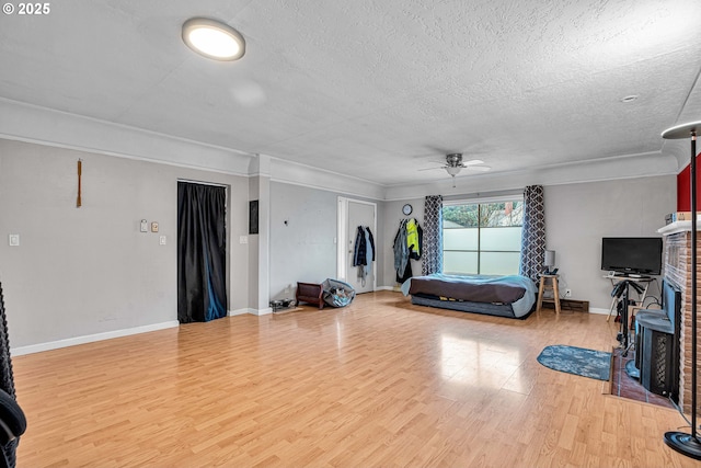 living room featuring crown molding, a brick fireplace, a textured ceiling, light wood-type flooring, and ceiling fan