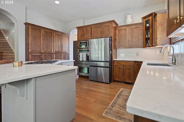 3534 NW Maple St, Camas, WA 98607 - kitchen with appliances with stainless steel finishes, a sink, arched walkways, light stone countertops, and light wood-type flooring