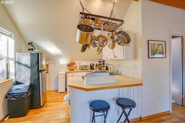 kitchen with a kitchen bar, vaulted ceiling, light wood-type flooring, stainless steel fridge, and kitchen peninsula