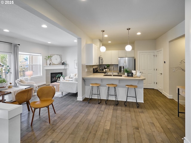 kitchen with tasteful backsplash, a glass covered fireplace, appliances with stainless steel finishes, wood finished floors, and a peninsula