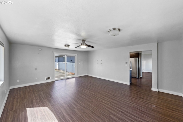 unfurnished living room featuring baseboards, dark wood-style flooring, ceiling fan, and visible vents