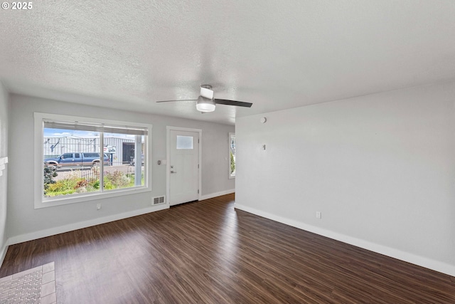 unfurnished living room featuring a ceiling fan, baseboards, dark wood finished floors, and a textured ceiling