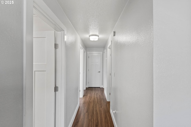 corridor with a textured ceiling, baseboards, and dark wood finished floors