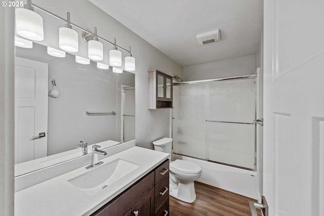 bathroom featuring vanity, enclosed tub / shower combo, wood finished floors, and toilet