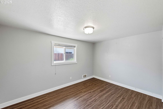empty room featuring a textured ceiling, baseboards, visible vents, and dark wood-type flooring
