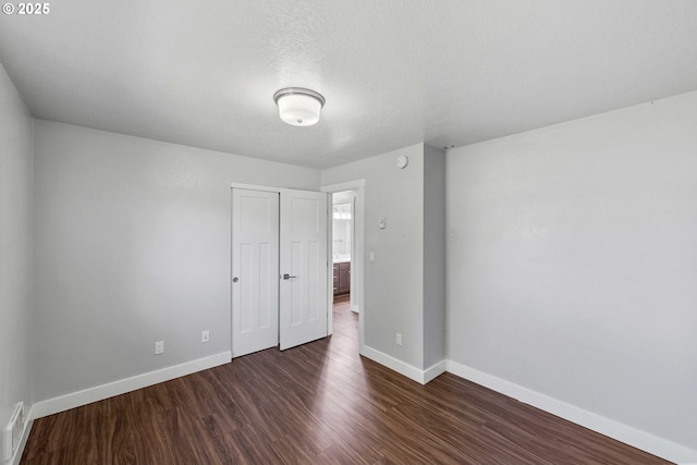 unfurnished bedroom with baseboards, dark wood finished floors, visible vents, and a closet