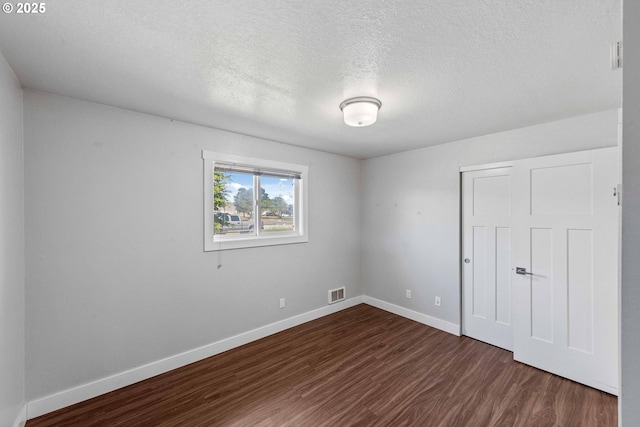 unfurnished bedroom with dark wood-style flooring, a textured ceiling, baseboards, visible vents, and a closet