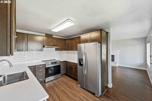 kitchen featuring light countertops, under cabinet range hood, tasteful backsplash, a sink, and appliances with stainless steel finishes