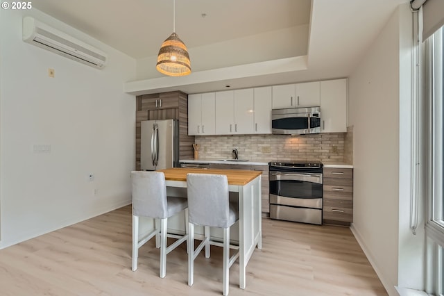 kitchen featuring appliances with stainless steel finishes, wood counters, an AC wall unit, tasteful backsplash, and light wood-style flooring