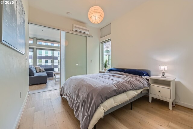 bedroom with a wall mounted air conditioner, light wood-style floors, and baseboards