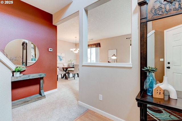 hallway featuring a chandelier, carpet flooring, and baseboards