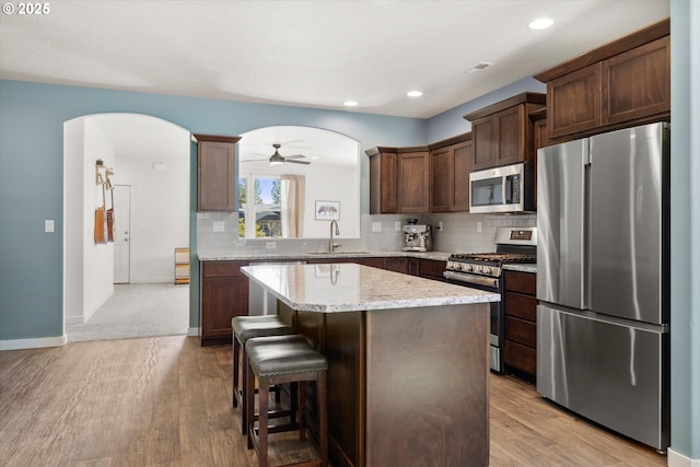 kitchen with light wood finished floors, a kitchen island, arched walkways, a sink, and appliances with stainless steel finishes