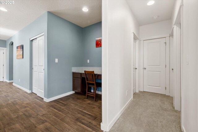 hallway featuring dark wood-type flooring, baseboards, recessed lighting, arched walkways, and a textured ceiling