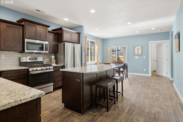 kitchen with visible vents, a kitchen island, dark brown cabinetry, wood finished floors, and stainless steel appliances