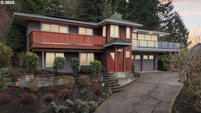 view of front of property featuring a garage, concrete driveway, a chimney, and a balcony