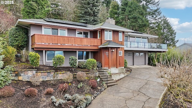 view of front facade with an attached garage, roof mounted solar panels, a chimney, and concrete driveway