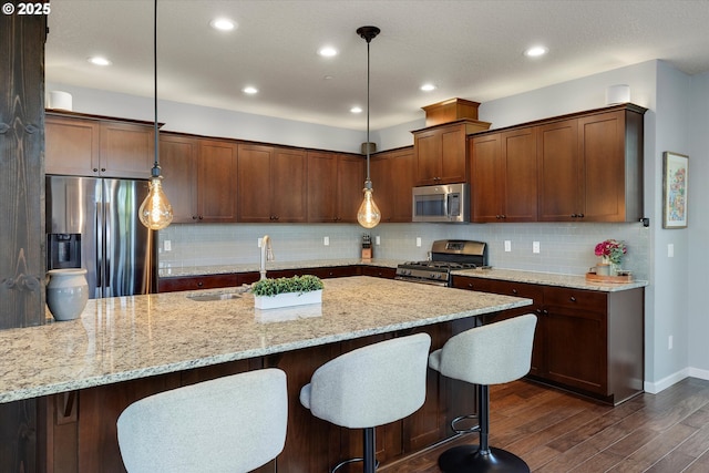10449 SW Denmark St, Wilsonville, OR 97070 - kitchen with stainless steel appliances, dark wood-style floors, light stone counters, a kitchen bar, and decorative light fixtures