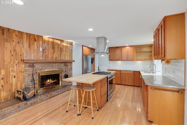 kitchen featuring island range hood, sink, butcher block counters, a kitchen bar, and premium appliances