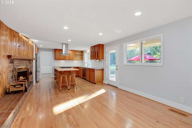 kitchen featuring light hardwood / wood-style flooring, a breakfast bar area, appliances with stainless steel finishes, a kitchen island, and island exhaust hood