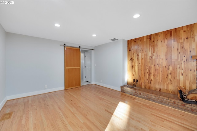 unfurnished room featuring a barn door, wooden walls, and light hardwood / wood-style flooring