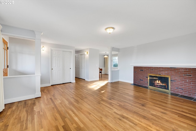 unfurnished living room with decorative columns, a brick fireplace, and light hardwood / wood-style flooring