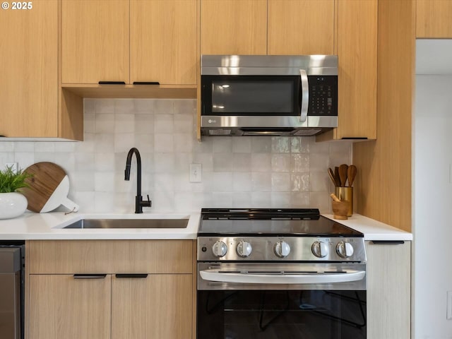 kitchen with appliances with stainless steel finishes, a sink, light countertops, and backsplash