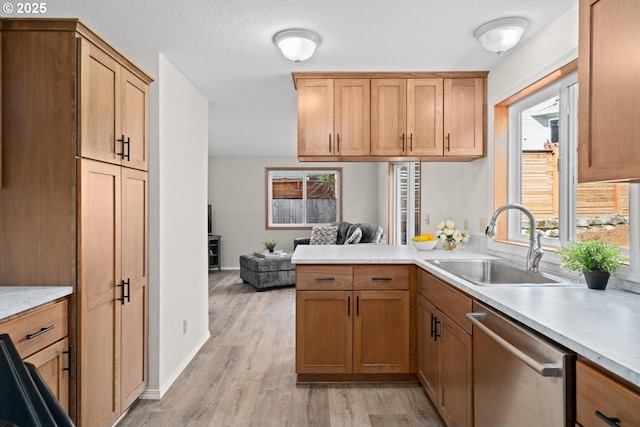 kitchen with dishwasher, a sink, light countertops, light wood-style floors, and a peninsula