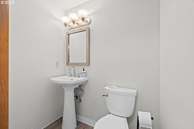 half bath featuring toilet, wood finished floors, baseboards, and a sink