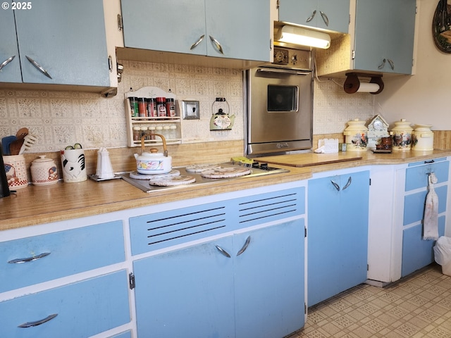 kitchen with stainless steel oven, backsplash, blue cabinetry, and white cooktop