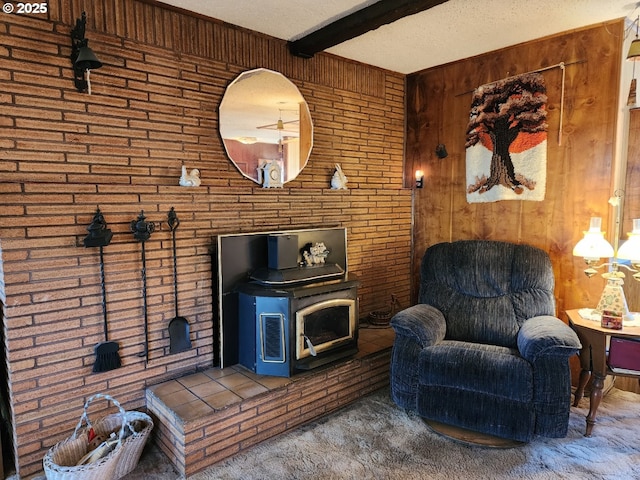 sitting room with carpet, beamed ceiling, wooden walls, a wood stove, and a textured ceiling